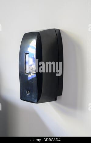 Automatic touch dispenser made of black plastic. A modern touchless hand sanitizer dispenser mounted on a white office wall. Stock Photo