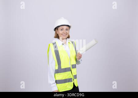 Smiling female architect holding paper rolls in hard hat Stock Photo