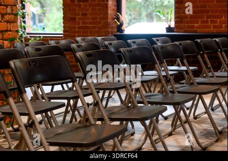 Rows of empty black folding chairs in a lecture hall with red brick walls.A multitude of folding chairs are set up for a seminar in the spacious inter Stock Photo