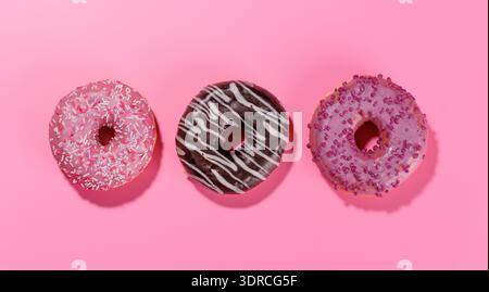 A colorful assortment of vibrant donuts with various toppings arranged on a pink Stock Photo