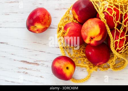 Nectarine. Ripe juicy organic nectarines (peaches) in a reusable mesh cotton shopping bag on a wooden table. plastic free zero w Stock Photo