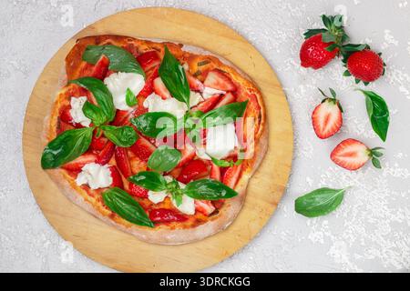 Homemade dessert pizza with tomato sauce, strawberries, burrata cheese and green Basil  close-up. Top view, selective focus Stock Photo