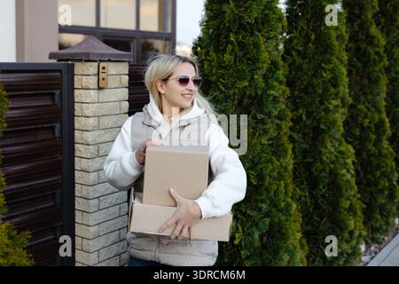 Courier delivering two cardboard boxes in front of a residential house gate, fulfilling ecommerce orders for customers in the neighborhood Stock Photo