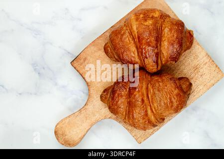 Freshly baked homemade croissants on a wooden cutting Board on a marble background.  Traditional breakfast. Selective focus, top Stock Photo