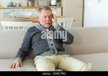 Headache pain. Unhappy middle aged senior man suffering from headache sick rubbing temples at home. Mature old senior grandfathe Stock Photo