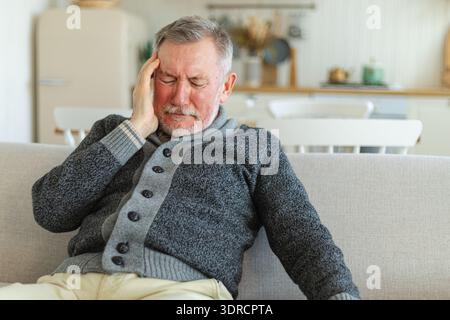 Headache pain. Unhappy middle aged senior man suffering from headache sick rubbing temples at home. Mature old senior grandfathe Stock Photo