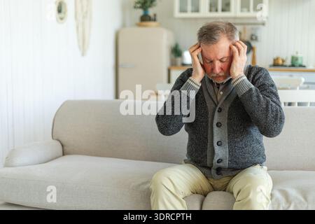 Headache pain. Unhappy middle aged senior man suffering from headache sick rubbing temples at home. Mature old senior grandfathe Stock Photo