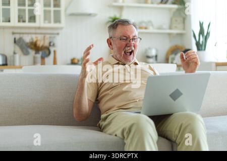 Excited middle aged senior man euphoric winner. Older mature grandfather looking at laptop reading great news getting good resul Stock Photo