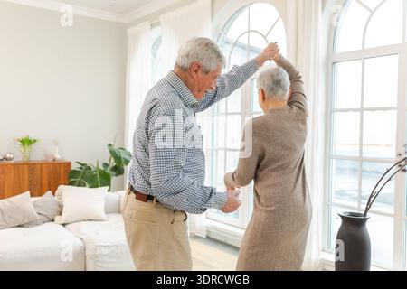 Keep moving. Romantic senior mature couple dancing to music together at home. Happy smiling family retired man woman husband wif Stock Photo