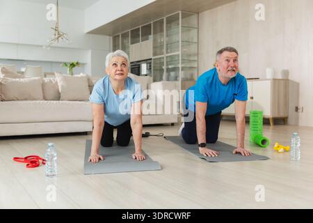 Fitness workout training. Senior adult mature healthy fit couple doing sports exercise on yoga mat on floor at home. Mid age old Stock Photo