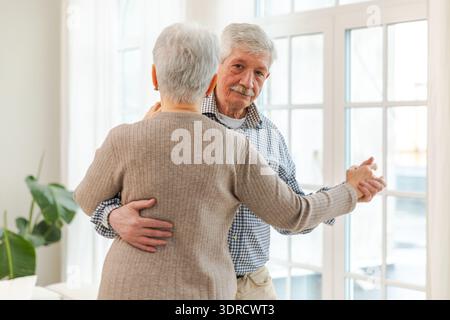 Keep moving. Romantic senior mature couple dancing to music together at home. Happy smiling family retired man woman husband wif Stock Photo