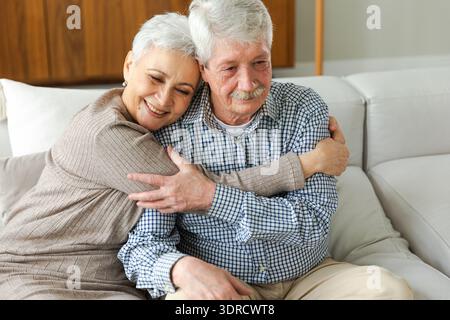 Senior adult mature couple hugging at home. Mid age old husband and wife embracing with tenderness love enjoying sweet bonding w Stock Photo