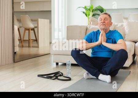 Yoga mindfulness meditation. Senior adult mature man practicing yoga at home. Mid age old grandfather sitting in lotus pose on y Stock Photo