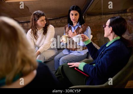 Women discussing ideas while holding coffee during team meeting. Stock Photo