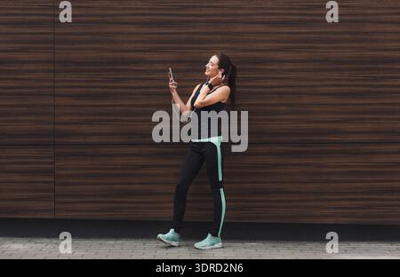 Woman Listens to Music While Using Phone Near Wooden Wall in Urban Setting Stock Photo