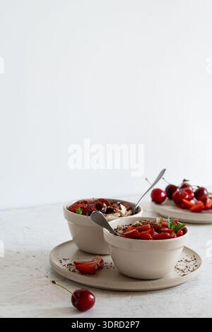 Multigrain oatmeal bowls with fresh strawberries, sweet cherries, berry jam, and almonds. Healthy breakfast porridge, side view with copy space Stock Photo