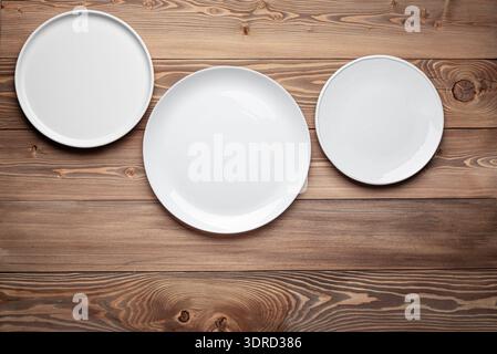 Three empty white plates on wooden table background Stock Photo