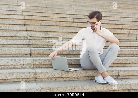Man Sitting on Stairs Using Laptop and Talking on Phone During Daytime Stock Photo