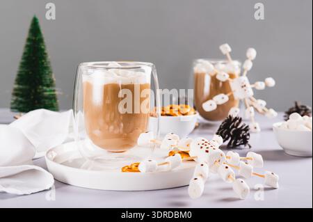 Warm cocoa in cups and snowflakes made of marshmallows and icing on a plate on the table Stock Photo