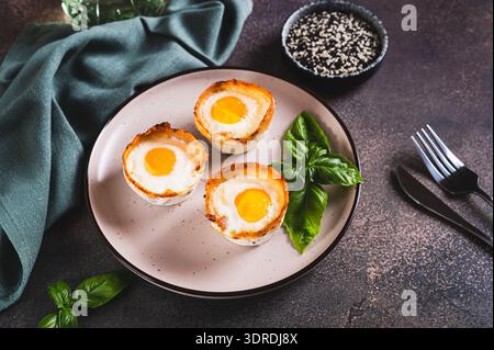 Baked egg and bacon rolls with basil on a plate on a table Stock Photo
