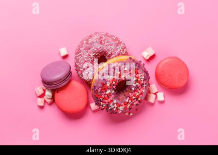 An eye-catching arrangement of colorful macarons and donuts on a pastel pink background Stock Photo