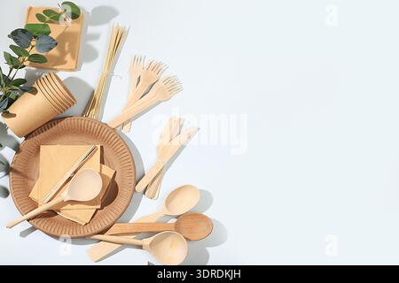 A set of environmentally friendly dishes on a sunny table. Paper cups, plates, kraft paper napkins, barbecue straws, wooden fork Stock Photo