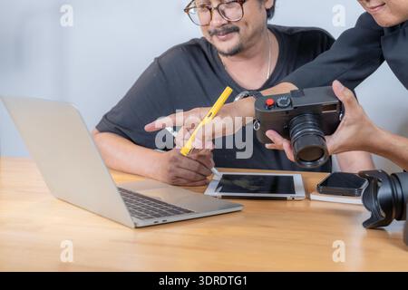 Two young photographers review images on a computer in their studio, highlighting teamwork, creativity, and professional photo editing workflow. Stock Photo