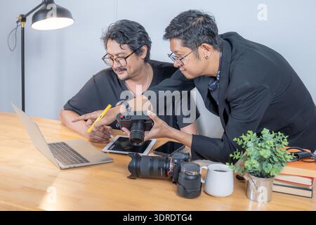 Two young photographers review images on a computer in their studio, highlighting teamwork, creativity, and professional photo editing workflow. Stock Photo