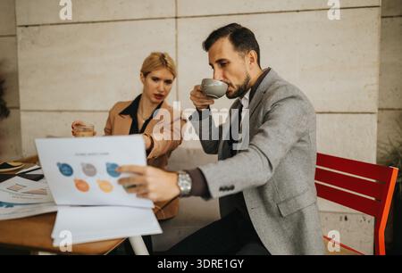 Business partners review charts and documents over coffee in a casual cafe setting Stock Photo