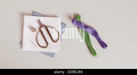 Canvas, threads and cross stitch tools on gray background top view web banner Stock Photo