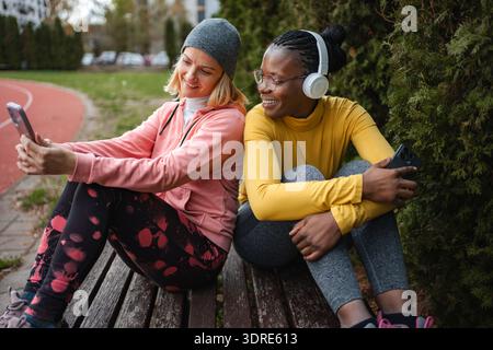 Diverse women friends resting on bench using smartphone Stock Photo