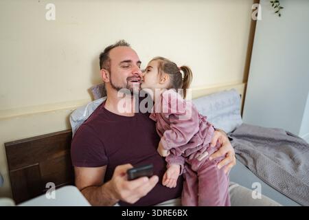 Happy father receiving daughter's kiss using smartphone Stock Photo