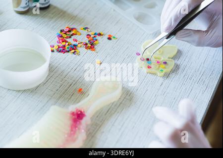 A girl in gloves uses tweezers to place elements into a mold for making earrings from epoxy resin Stock Photo
