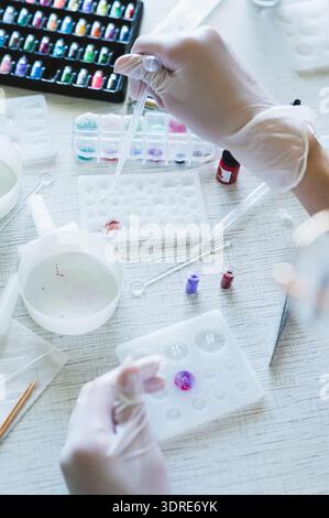 Children's hands in gloves fill a crystal mold with epoxy resin from a pipette vertical view Stock Photo