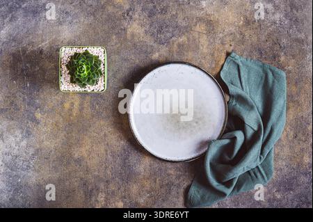 Ceramic empty plate, napkin and potted succulent on textured gray background top view Stock Photo