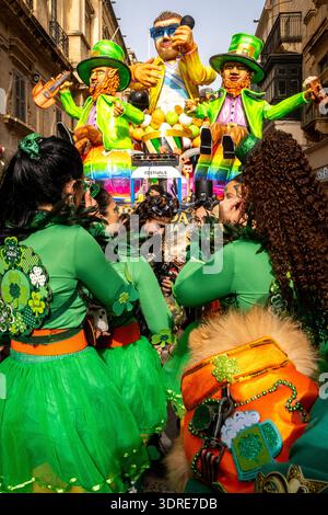 People in green costumes with shamrock decorations gather in front of a giant parade float marked FESTIVALS Malta during Malta Carnival in Valletta, M Stock Photo