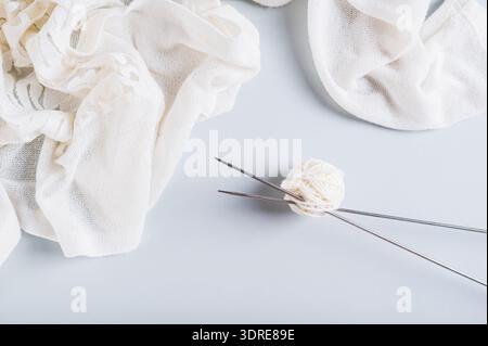 Knitting needles stick out from a ball of yarn and knitted fabric nearby on a blue top view Stock Photo