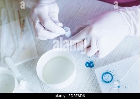Female hands in gloves pour sparkles into a mold for making a pendant from epoxy resin Stock Photo