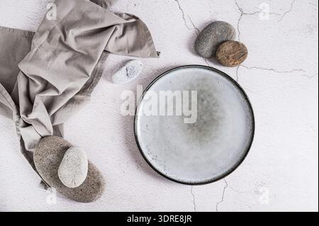 Empty ceramic plate, stones and napkin on gray background top view Stock Photo