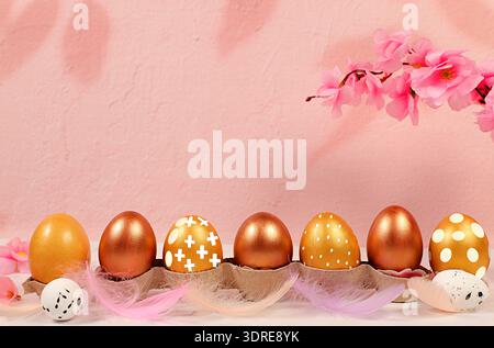 Golden Easter eggs, painted for the holiday, on a pink background with a sakura branch. Happy Easter concept. Abstract Easter co Stock Photo