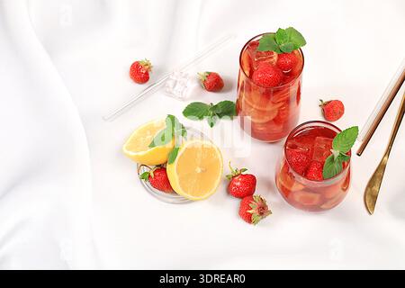 Strawberry Iced Tea or Mint Lemon Cocktail is a refreshing summer drink recipe. Glasses with berry fruit lemonade on a light con Stock Photo