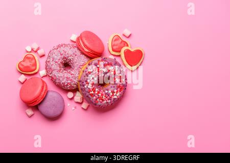 An eye-catching arrangement of colorful macarons and donuts on a pastel pink background Stock Photo