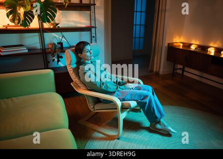 Thoughtful senior woman sitting alone in room in rgb light, coping with loneliness after divorce. Stock Photo