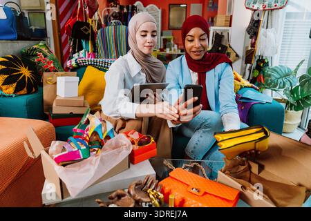 Two diverse women wearing hijabs developing their e-commerce business, sharing new fashion shoes and accessories through a live streaming video on a s Stock Photo
