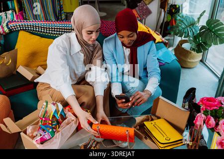 Two diverse women wearing hijabs developing their e-commerce business, sharing new fashion shoes and accessories through a live streaming video on a s Stock Photo