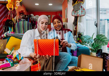 Two diverse women wearing hijabs developing their e-commerce business, sharing new fashion shoes and accessories through a live streaming video on a s Stock Photo