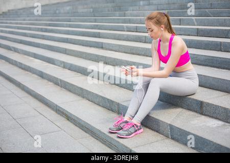 Young Woman Sits on Steps Listening to Music With Her Phone in the City Stock Photo
