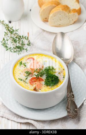 Salmon creamy soup with vegetables - potatoes, carrots, tomatoes and broccoli in a white bowl on bright wooden table Stock Photo
