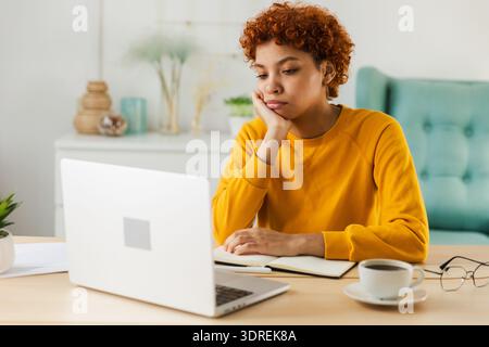 Sleepy sad african american woman sitting at table with laptop. Tired overworked girl lazy to work. Student businesswoman relaxi Stock Photo