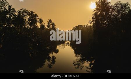 Serene sunset over tranquil river in Chumphon Thailand surrounded by lush palm trees Stock Photo